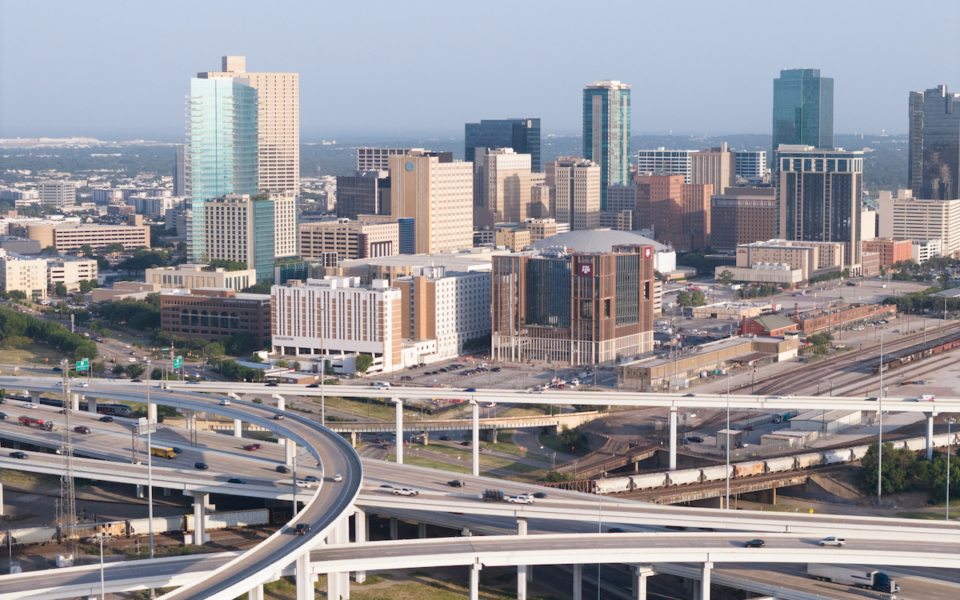 A bustling urban skyline with modern skyscrapers overlooks a complex network of elevated highways and overpasses.