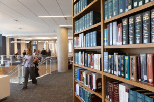 A person walks through a modern library with tall wooden bookshelves filled with legal texts and books.